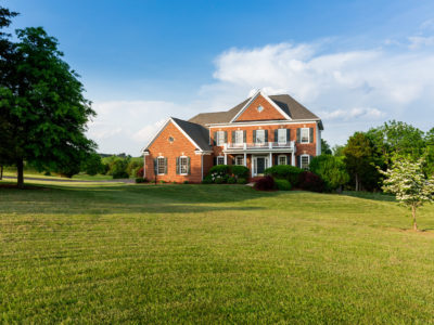 Front of home and garage of large single family modern US house with landscaped gardens and lawn on a warm sunny summers day