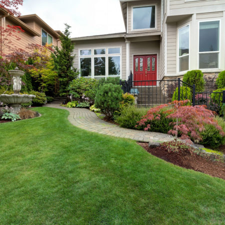Frontyard garden of house with water fountain green grass lawn paver brick path trees and shrubs landscaping